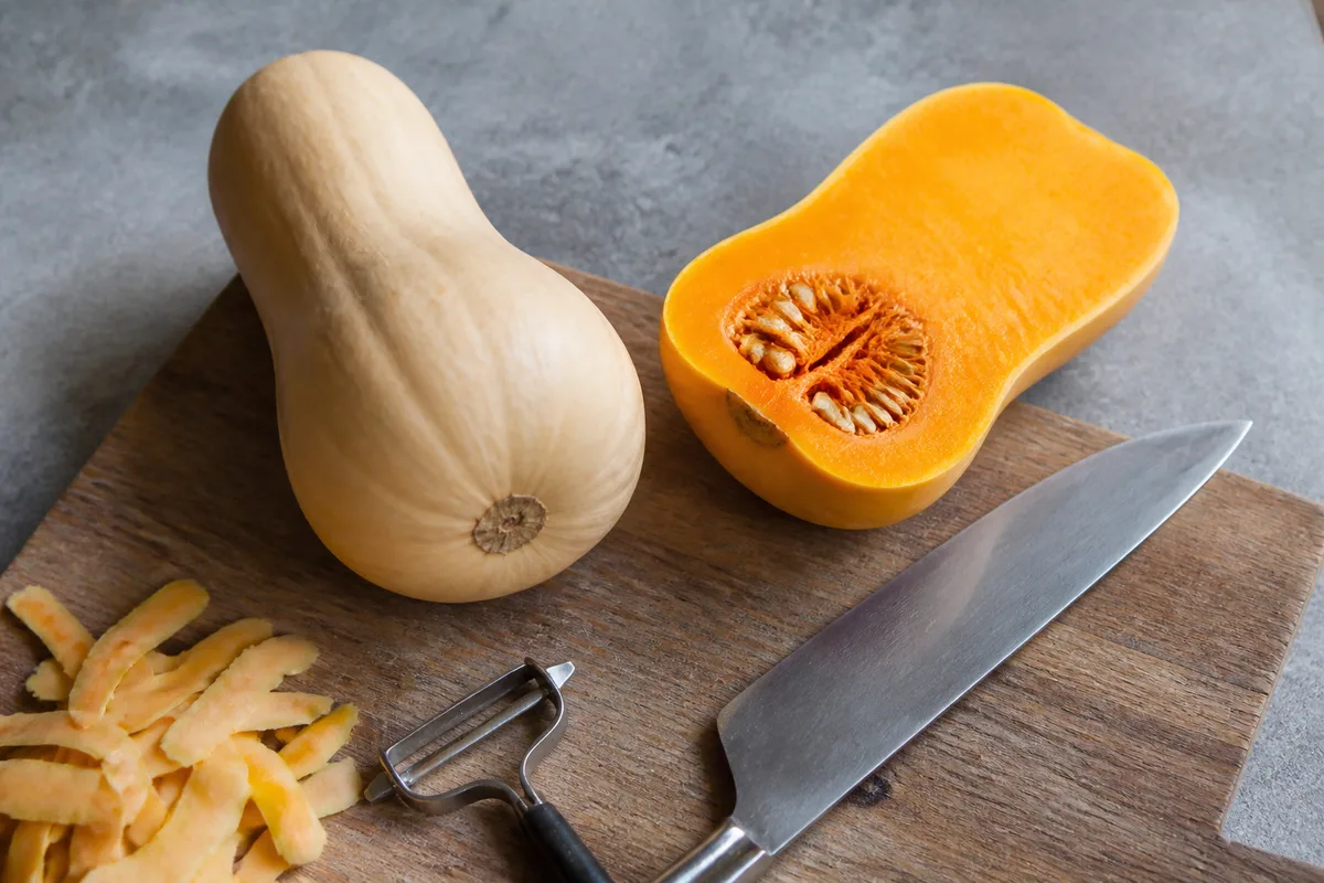 Courge butternut entière posée sur une planche en bois à côté d un économe
